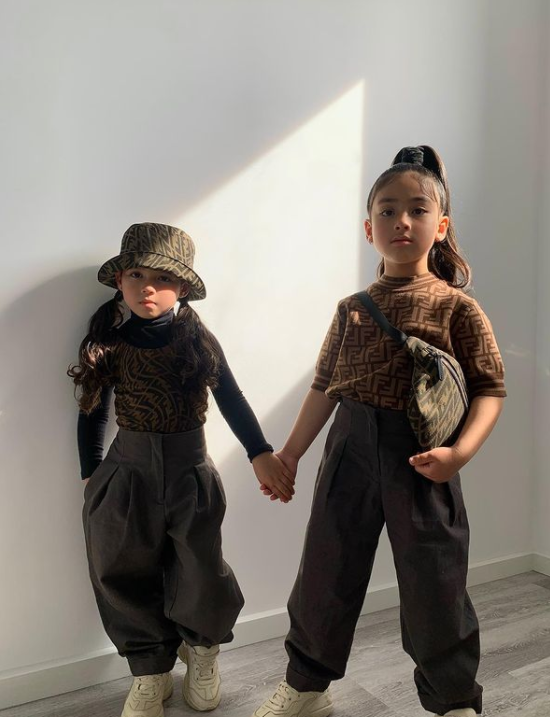two little girls holding hands and wearing identical outfits posing in front of a blank wall