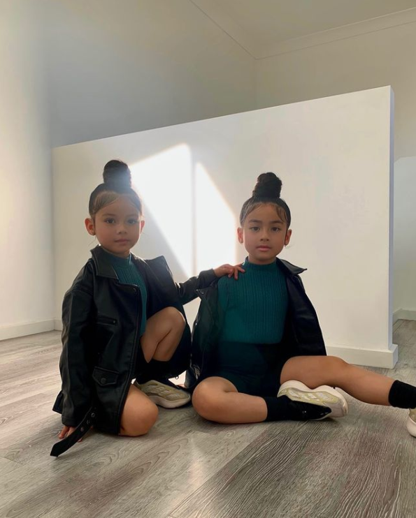 two little girls wearing matching outfits and sitting on the floor inside an empty room