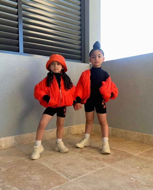 two little girls holding hands and wearing matching outfits while posing outside