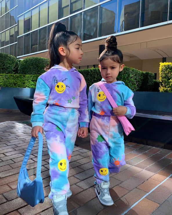 two little girls wearing colorful matching outfits and walking while holding hands