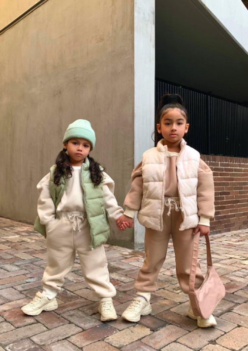 two little girls holding hands and wearing neutral outfits outside