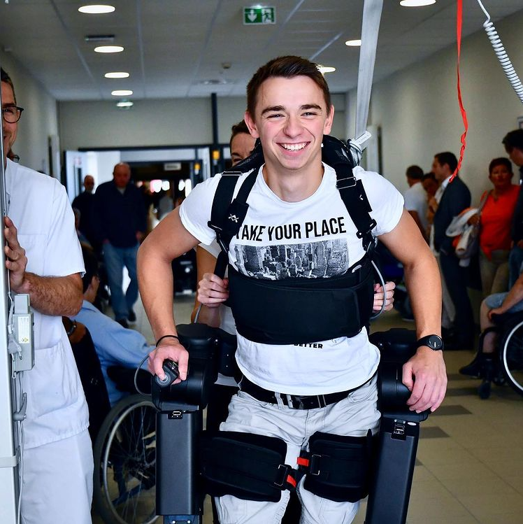 teenager smiling wide and walking with a robotic exoskeleton