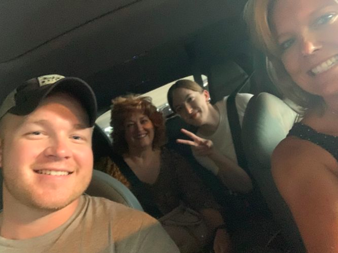 man smiling in passenger seat of car beside three women