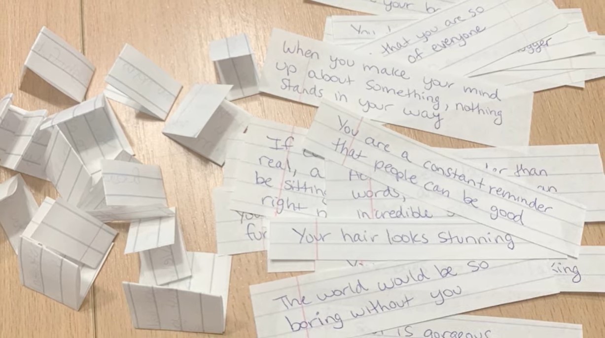 folded pieces of torn paper next to opened up pieces of torn paper with compliments written on them