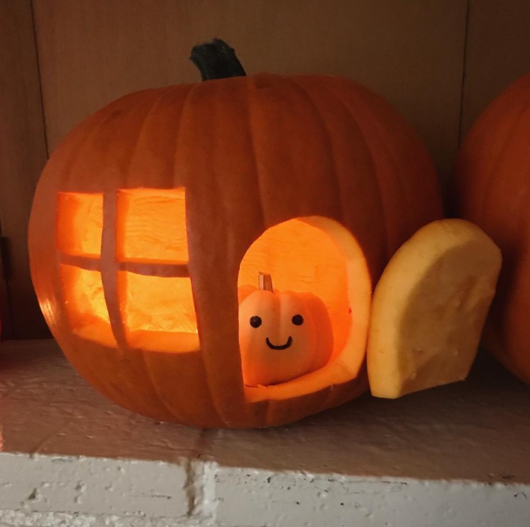 small carved pumpkin with a window and an open front door with an even smaller pumpkin inside with a smiley face drawn on with a black marker