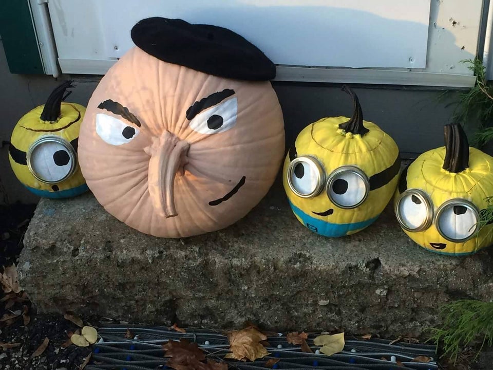 large pumpkin designed to look like gru from despicable me next to three small pumpkins designed to look like the minions from the movie despicable me