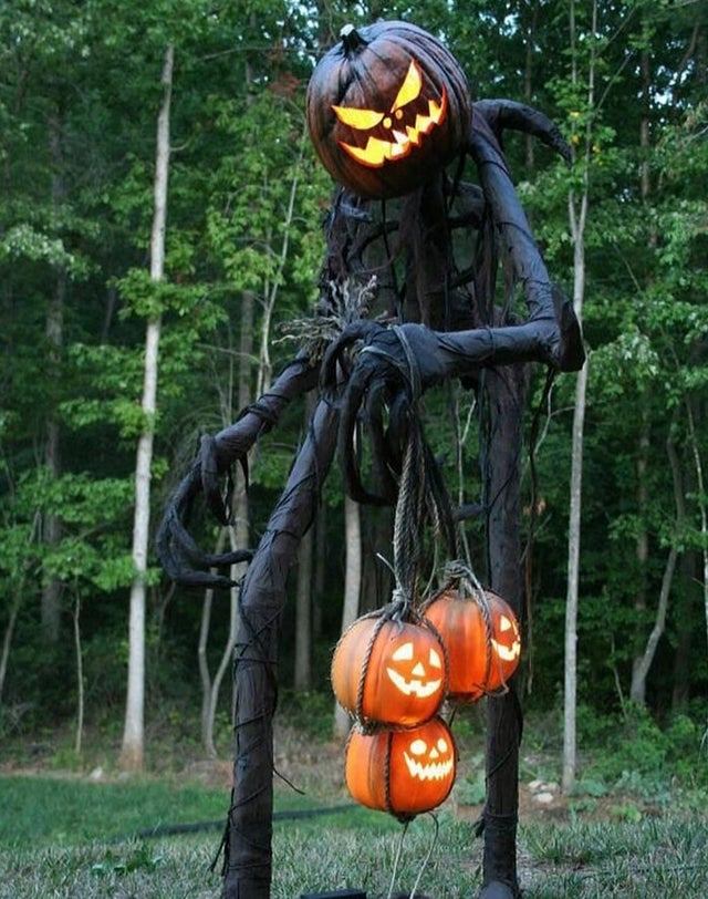 super tall outdoor halloween decoration with a carved pumpkin head that is carrying smaller carved pumpkins 