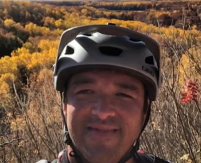 closeup of a man smiling while wearing a bike helmet and standing outside 