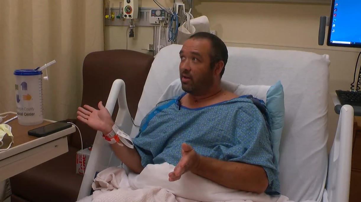 man sitting up in a hospital bed talking and gesturing with his hands