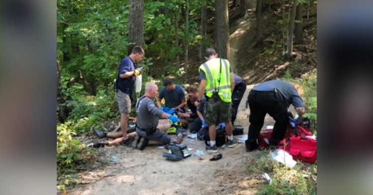 team of paramedics assisting a man laying on the ground in a wooded area