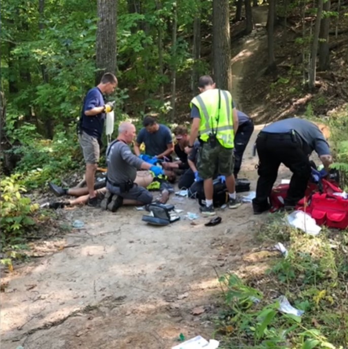 team of paramedics assisting a man laying on the ground in a wooded area