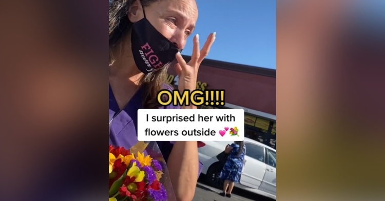 woman who is wearing a face mask and holding flowers standing outside of a grocery store and crying