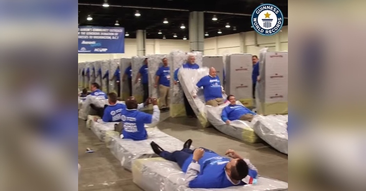 aaron's employees laying on and standing in front of upright mattresses to beat guinness world record for human matress dominoes