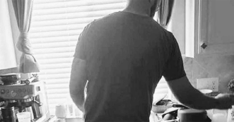 black and white photo of man standing in kitchen with back to camera