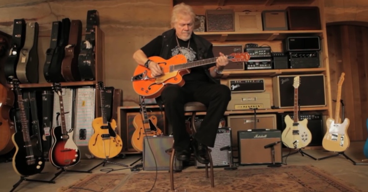 randy bachman sitting on a stool surrounded by guitars and playing a 1957 gretsch 6120 chet atkins guitar