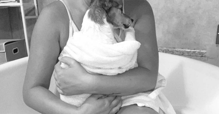 black and white photo of woman holding small dog in bathtub
