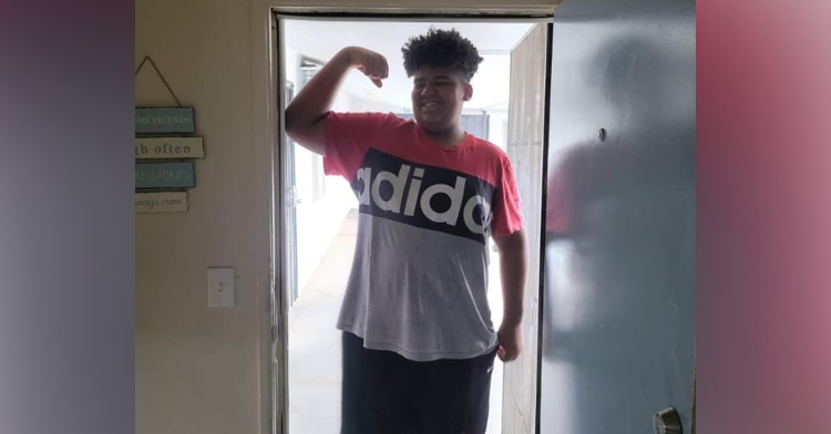 tall 12 year old boy standing in the doorway of a house while smiling and flexing his arm muscles