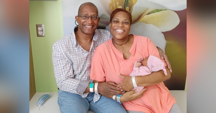 man named tony troxler sitting with his arms around his wife, susie troxler, who is holding their baby girl, lily troxler