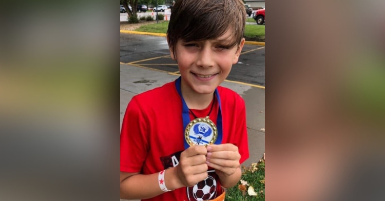 9 year old kade lovell smiling while showing off the medal he won for getting first place in a 10k race
