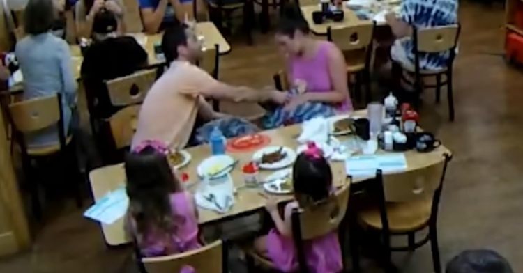 family of five sitting at a table in a restaurant while the mom and dad try to help their choking baby