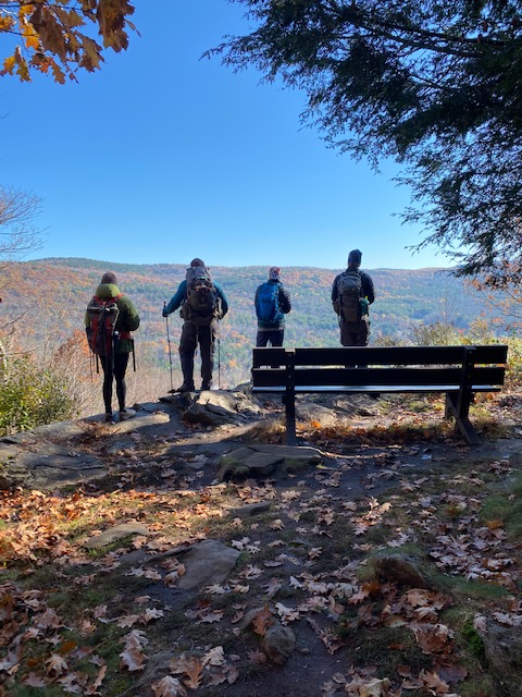 group of four hikers standing on the edge of a mountain and looking at the scenery