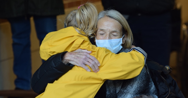 woman wearing a mask and sitting in a wheelchair hugging a little girl tightly