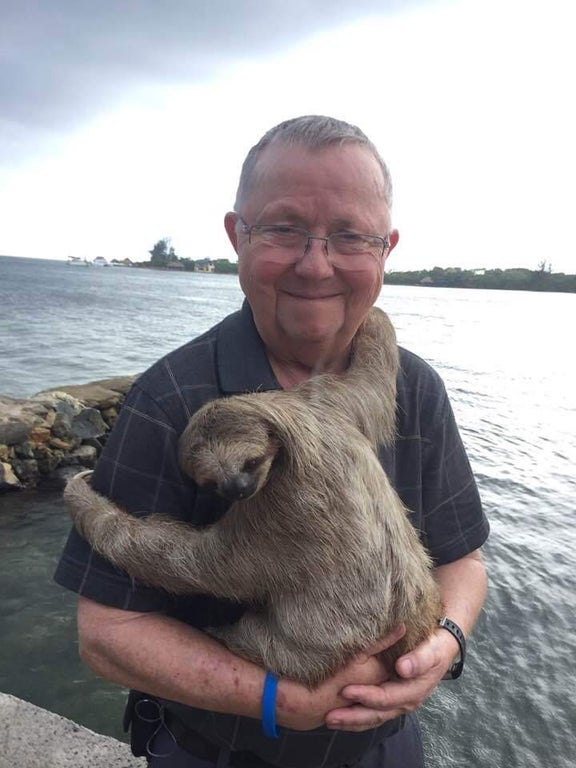 elderly man holding and hugging a sloth while standing by the water