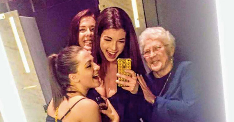 three young women posing with grandma in front of mirror