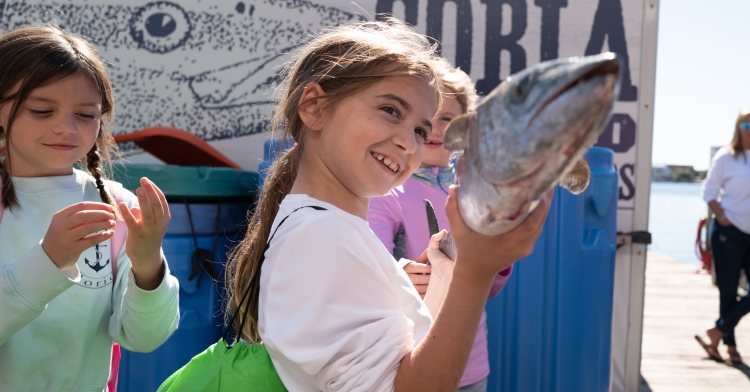 two little girls smiling and holding a huge fish they caught while standing on a dock for take-a-kid-fishing day in destin, florida