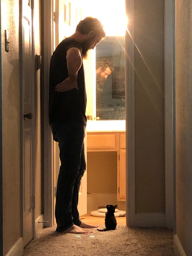 man standing in doorway with tiny kitten at his feet
