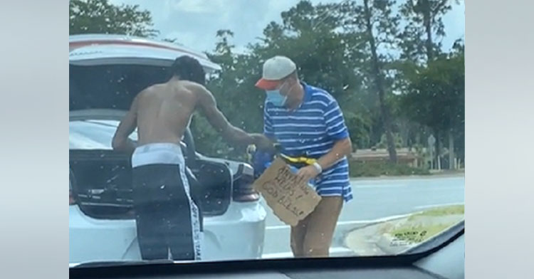 college student standing next to open car trunk with homeless man
