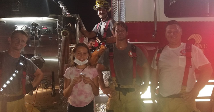 little girl standing in front of fire truck with firefighters