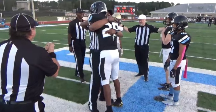referees and high school football players standing around foorball player fred grooms ii hugging his dad major fred grooms jr who is dressed as a referee