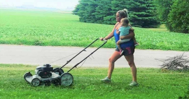 mom holding baby while mowing the lawn