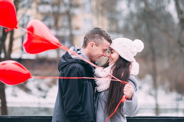 man and woman about to kiss holding red heart-shaped balloons