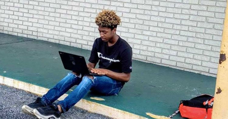 student sitting on sidewalk with open laptop