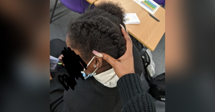 8 year old purity agyeman sitting in a chair as her teacher vanessa sefa uses her hand to show off the little girl's hair which has been styled into two cornrows