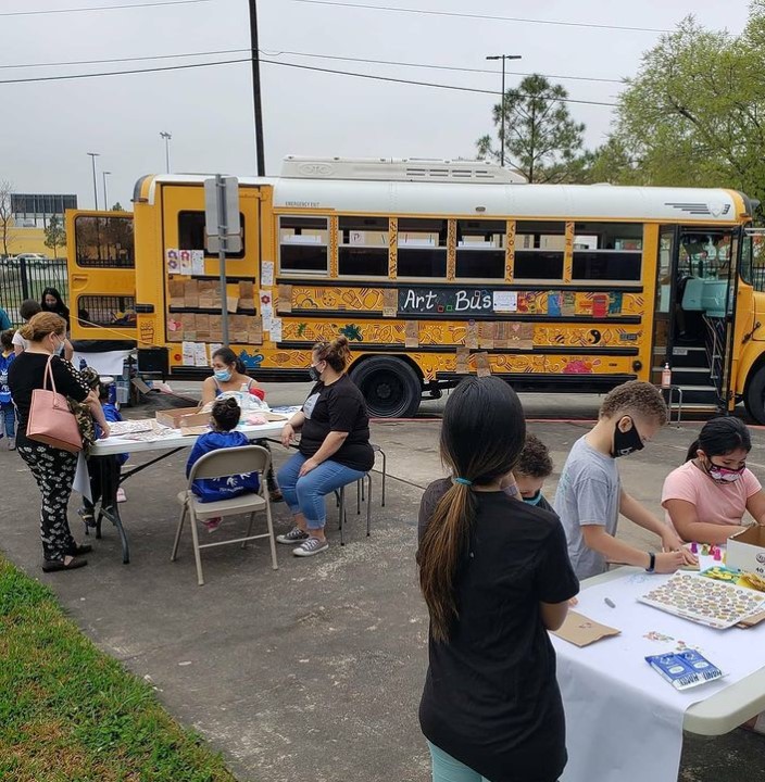 people gathered around tables outside of a renovated school bus called the "art bus" by htx art