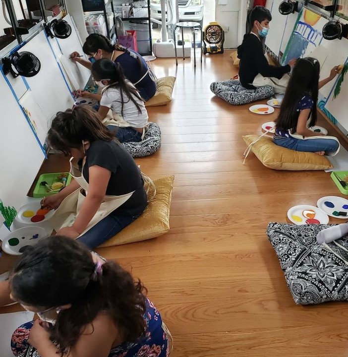 group of children sitting on cushions while painting on canvas inside of a mobile art bus from htx art