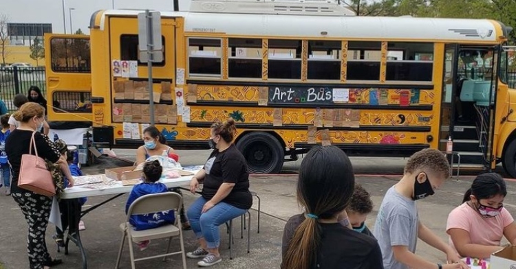 people gathered around tables outside of a renovated school bus called the "art bus" by htx art
