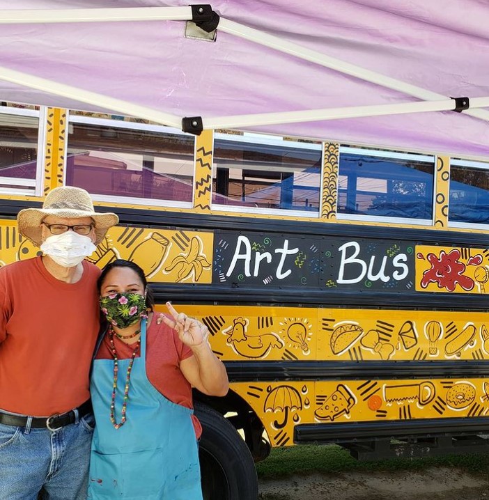 man and woman wearing face masks while they pose in front of a renovated school bus that's been turned into an 