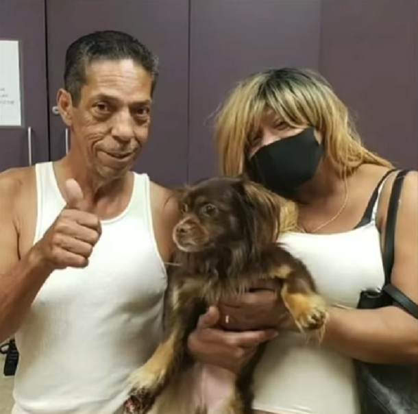 man with thumbs up next to woman holding small brown dog