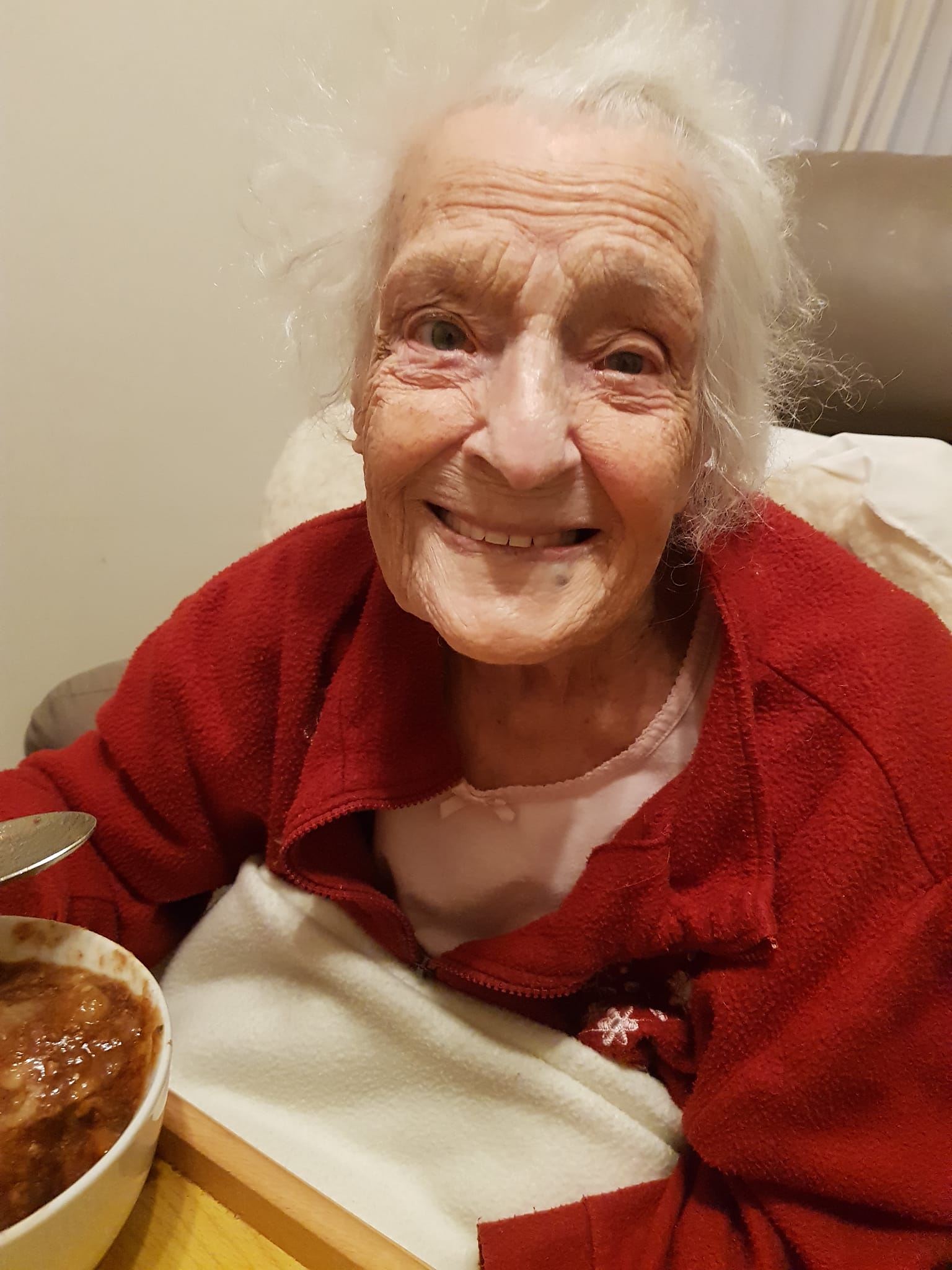 elderly woman named lilian howitt sitting in a chair with a bowl of soup and smiling