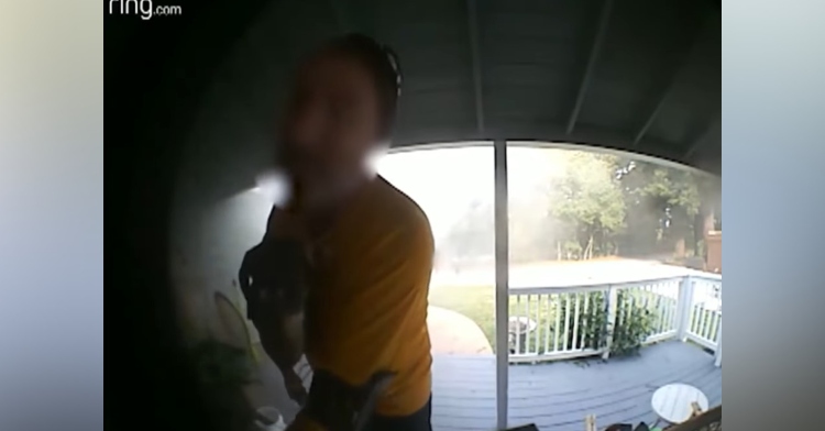 man with his face blurred out standing on a front porch carrying a dog in his arms from the view point of a ring camera