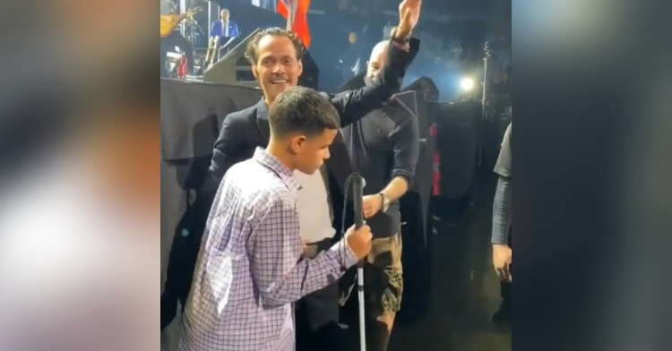 marc anthony waving to the crowd at his concert as he stands with a 16 year old fan named johnny rivera jr who is blind