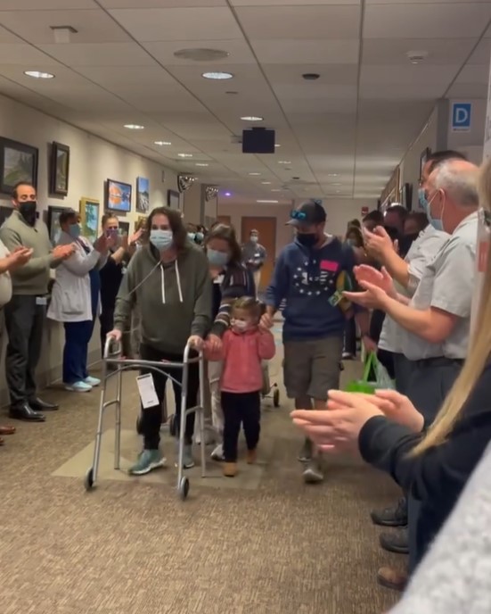 group of people gathered in bryn mawr rehab hospital clapping and cheering as a woman named marissa fuentes is leaving the rehab center with her husband, toddler, and baby by her side