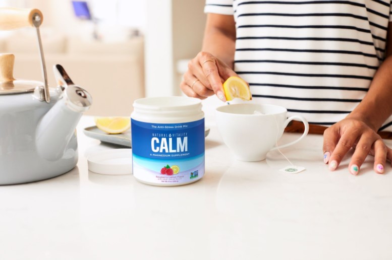 closeup of a counter where a woman is squeezing a lemon into a cup next to a container of natural calm raspberry lemon flavor by natural vitality