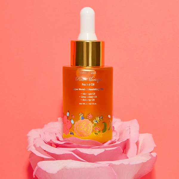 bottle of rose moringa facial oil from winky lux sat on top of a pink flower