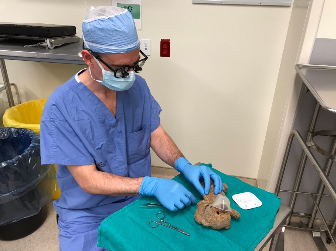 doctor dressed for surgery as he pretends to perform surgery on a child's teddy bear