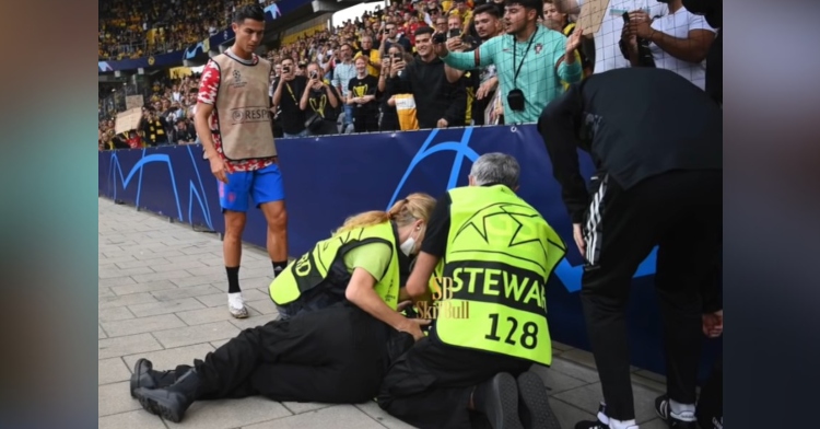 soccer player cristiano ronaldo standing by and looking at a group of medics who are examining a steward who is laying on the ground